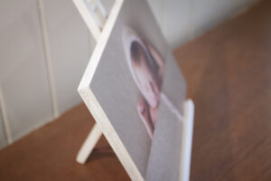 Close up of the corner of a white wash edge block mount resting on a white photo easel on a wooden table with an image of a newborn baby