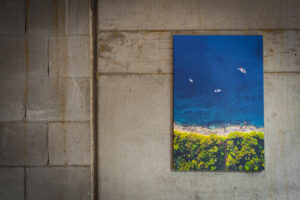 Aerial shot of boats moored near shore printed with vibrant colours and mounted on 12mm block mount with black edge hung on an industrial concrete wall