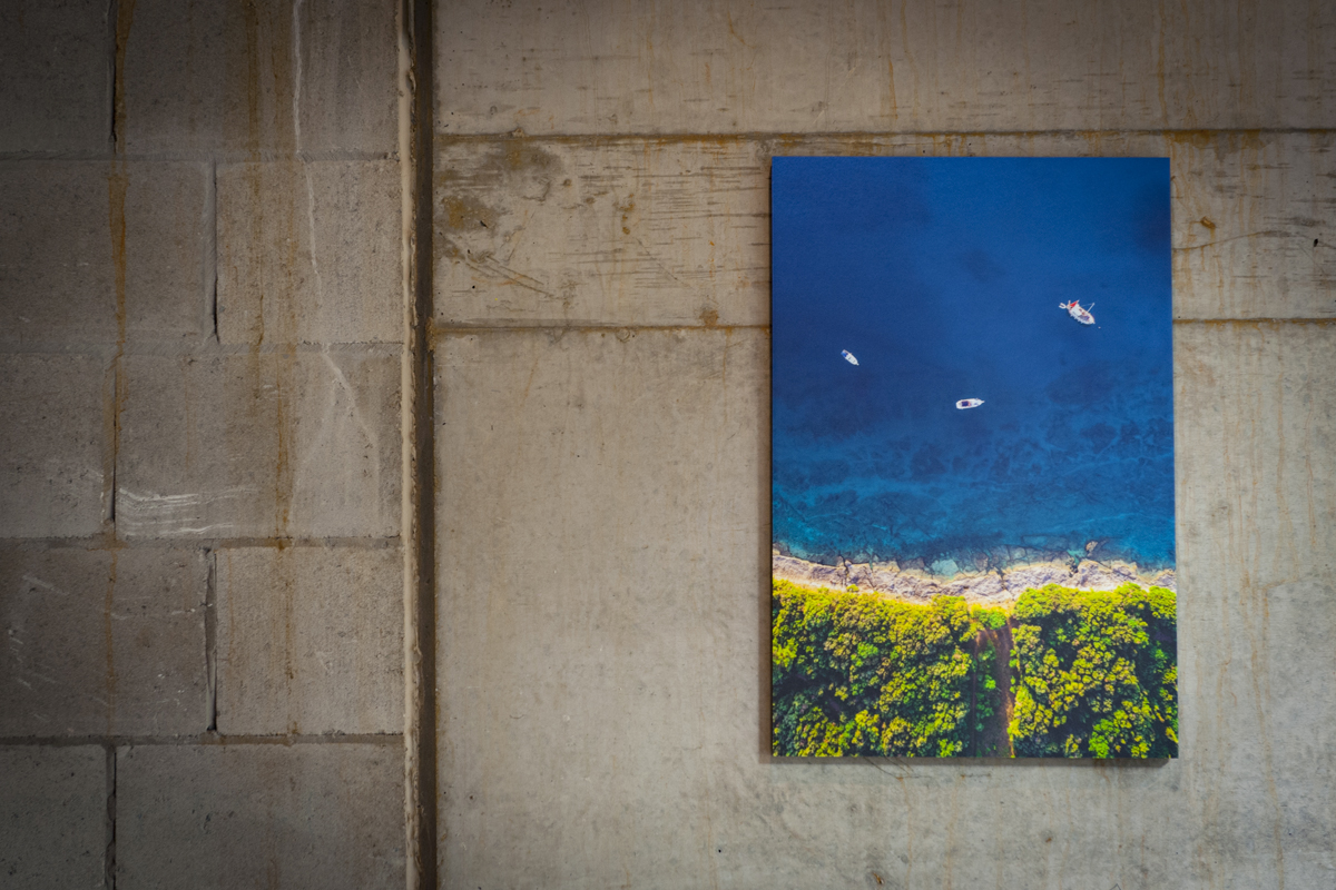 Aerial shot of boats moored near shore printed with vibrant colours and mounted on 12mm block mount with black edge hung on an industrial concrete wall