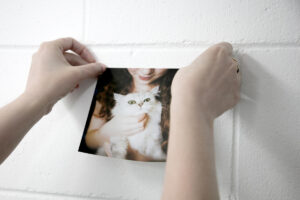 Hands placing a photo wall sticker of a girl holding a cat onto a white brick wall