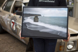 Photo lab staff holding a black float framed canvas image of a beach with black sand