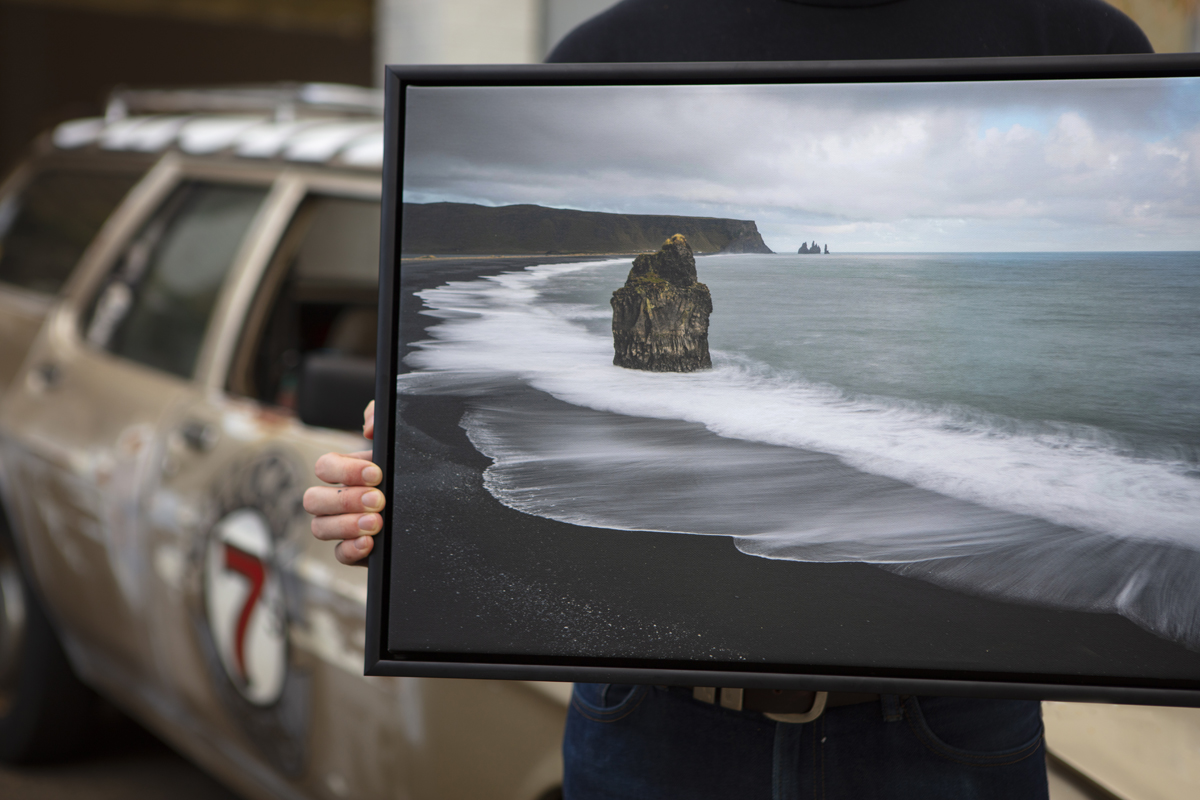 Photo lab staff holding a black float framed canvas image of a beach with black sand