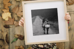 Girl holding an oak framed black and white image of a boy and girl with a white matt