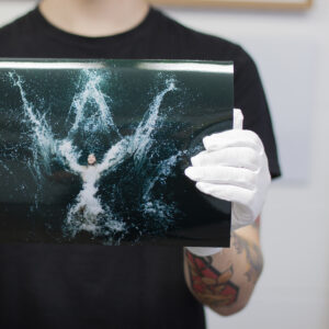 Photo lab staff wearing white cotton gloves holding a glossy print of a man swimming