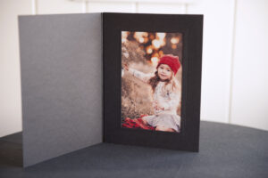 Black slip-in photo folder with lustre photograph of young girl displayed inside and sitting up on black table