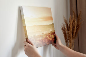 Hands hanging a small canvas print with gallery wrap of a landscape on white wall