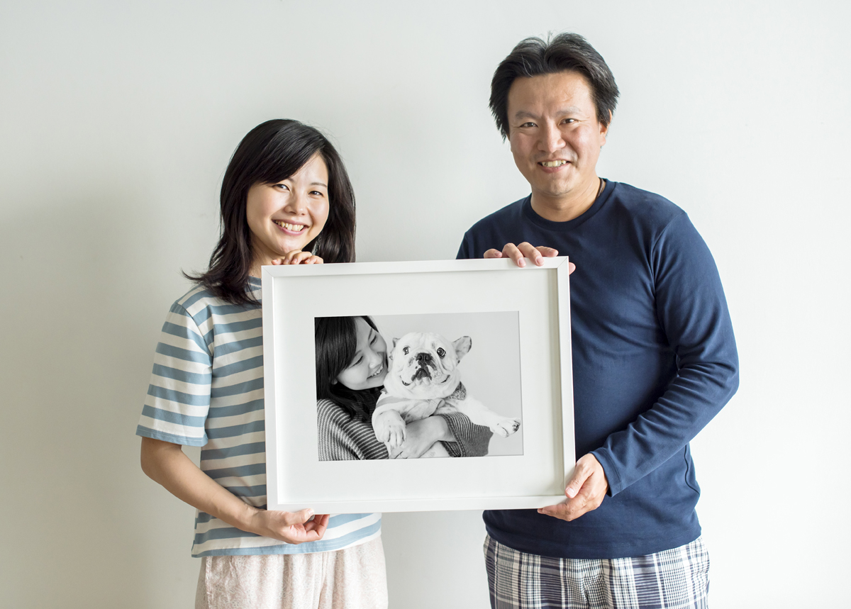 Asian couple holding a white framed print of a woman and her dog