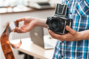 Photographer standing with retro medium format camera and negative film. Unrecognizable man holding old fashioned photographing equipment. Electronic development, technology evolution, hobby concept