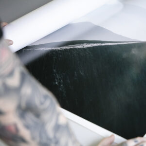 Man with tattooed arms rolling out a large lustre print of a mountain on a table