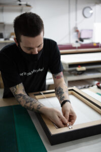 Lab staff reaches over to string up the hanger on the back of a framed canvas print