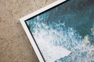 Corner of a white float framed canvas print image of a beach