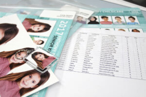 Pile of prints, photo keyring and printed spreadsheet ready for sorting school photos into packs