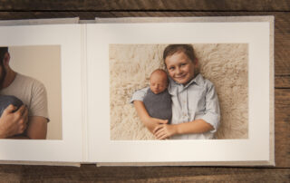 Linen photo album open on wooden box to a page with a printed photo of a boy and his baby brother